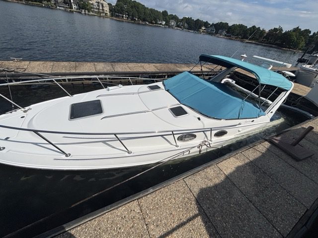 A white luxury motorboat docked at a waterfront marina on a sunny day.