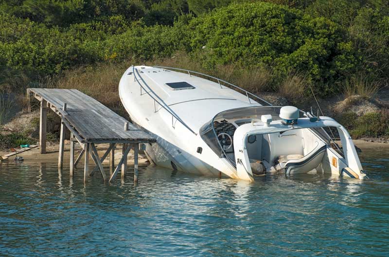 A white boat partially capsized near a wooden dock in calm water.