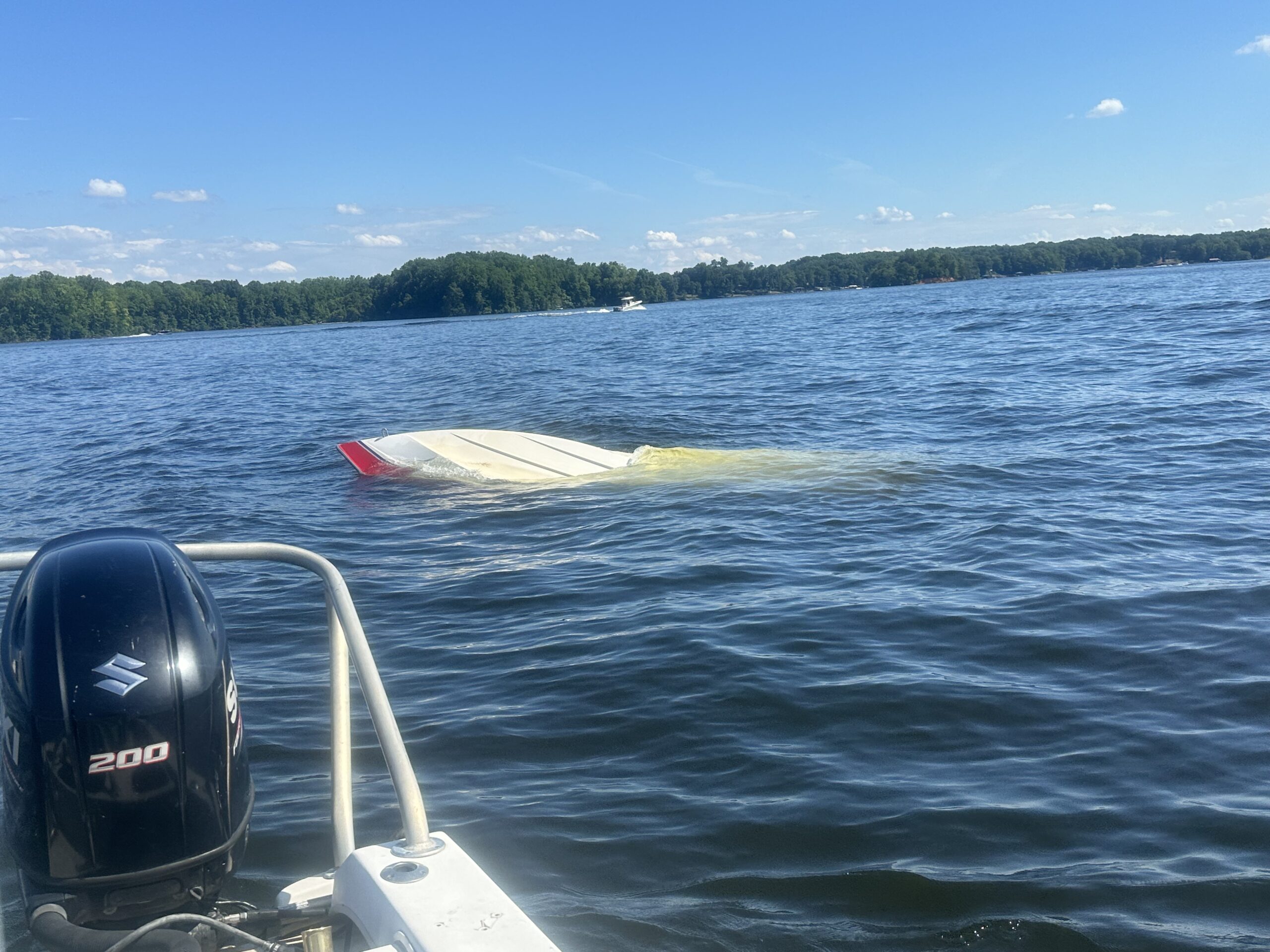 Capsized boat floating upside down in a lake near a boat.